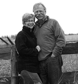 Picture of a man and woman leaning against a fence on a farm.