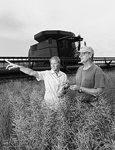 Man and woman standing in a field with combine tractor behind them.