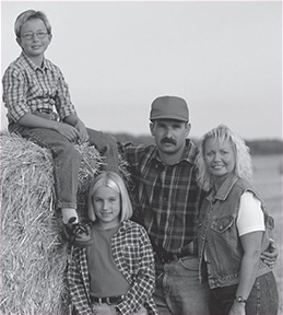 Portrait of a man, woman, and two children posing alongside a large bale of hay.